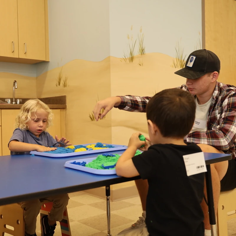 Alt text: "A volunteer plays with colored sensory dough alongside young kids in a children's ministry classroom at The Crossing in Milton, DE.